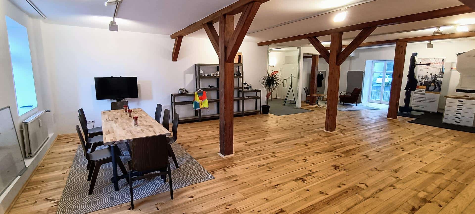 Heller Raum mit Holzfußboden, Tischen und Fahrradtrainingsbereich.