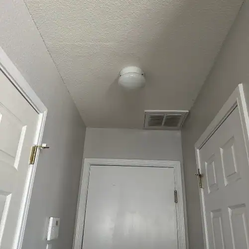 Subtle water stain on a hallway ceiling near a flush-mount light and return vent indicating need for roof leak repair San Antonio by Dolan Roofing & Construction in San Antonio