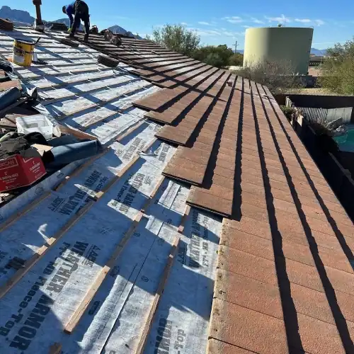 Roofing crew installing new underlayment and relaying clay tiles during roof replacement process in Texas