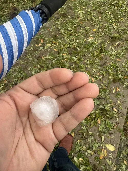 Hand holding large piece of hail over a shingle roof indicating hail size for hail damage repair San Antonio by Dolan Roofing & Construction