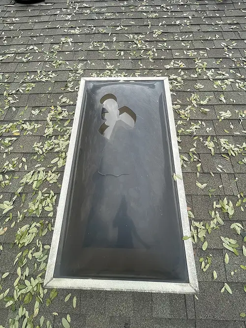 Close-up of skylight with visible damage surrounded by shingles following hail damage repair San Antonio by Dolan Roofing & Construction