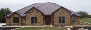 Front view of a single-story, light-brown stone house with a dark reddish-brown metal roof in San Antonio, TX