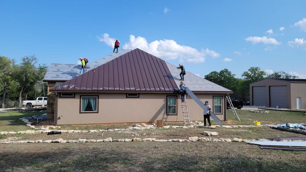 Workers installing durable metal roofing panels on a residential house by Dolan Roofing & Construction in San Antonio, TX.