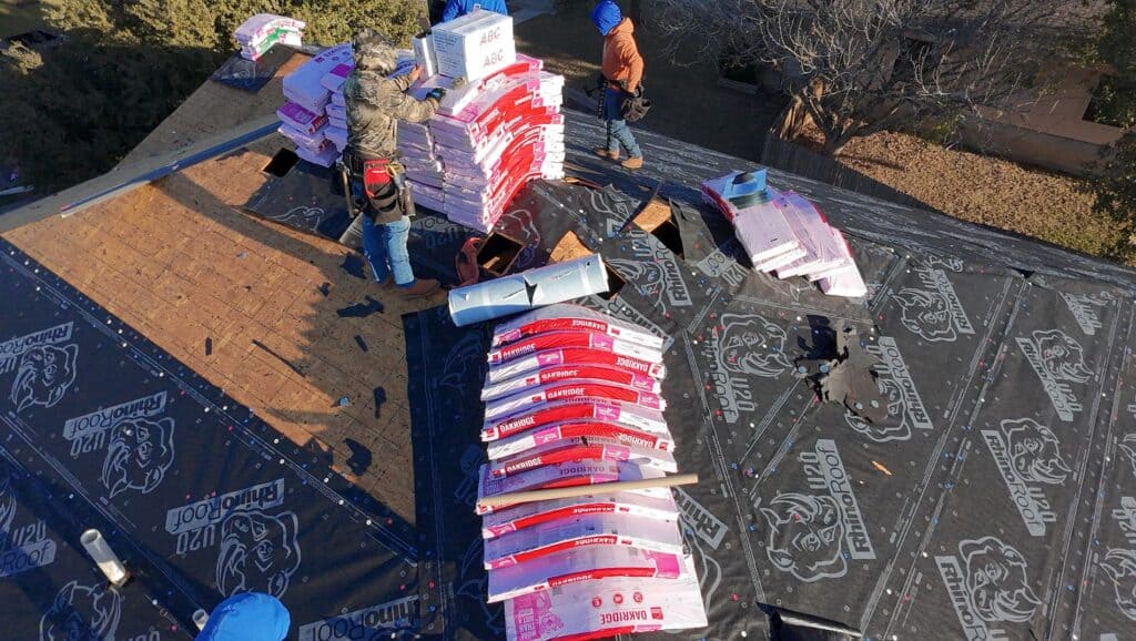 New asphalt shingle roof installation in progress with roofing experts at work.