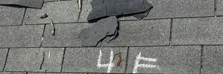 Damaged asphalt shingles on a residential roof with markings for inspection—illustrating the difference between actual cash value and replacement cost roof insurance in San Antonio.