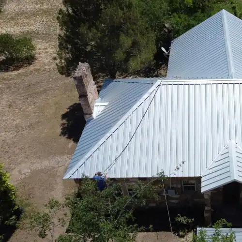 White standing seam metal roof installed on stone residential home, illustrating cost of metal roof San Antonio