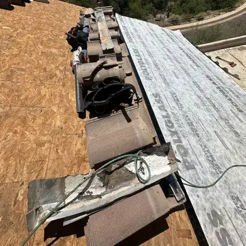 Roofing materials and tools on a roof, showing the installation of Polyglass underlayment for a tile roof by Dolan Roofing & Construction in San Antonio