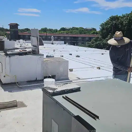 Installation crew applying white commercial roof coatings to flat roof with HVAC units in San Antonio, showing durability and energy efficiency by Dolan Roofing & Construction