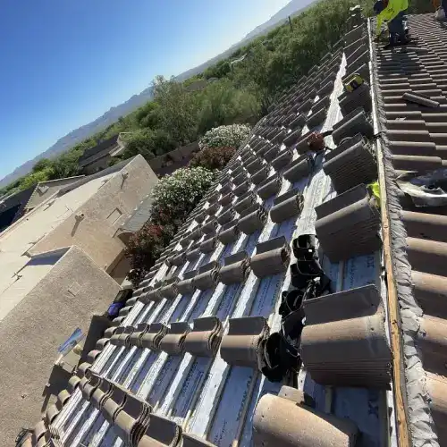  Tile roof lift and relay cost San Antonio showing stacked roofing tiles, exposed underlayment, and crew at work by Dolan Roofing & Construction in San Antonio