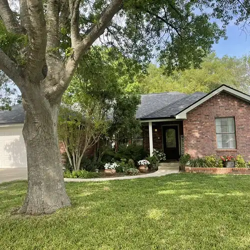 esidential home surrounded by trees with a clean, maintained roof after roof maintenance in New Braunfels by Dolan Roofing & Construction in Cibolo