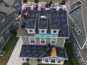 Dolan employees installing roofing materials on a house roof, with bundles of shingles visible across the surface in San Antoio