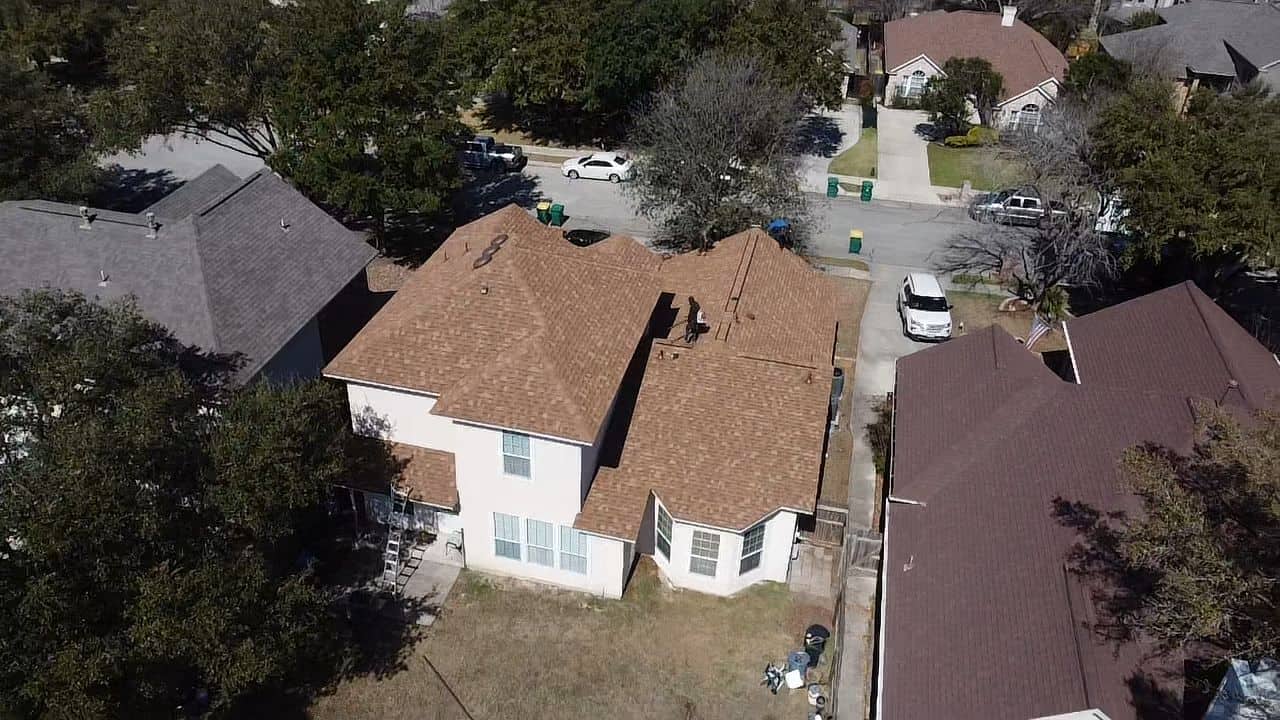 Aerial perspective of a two-story residential home with a completed brown shingle roof during a roofing replacement in Universal City TX by Dolan Roofing & Construction