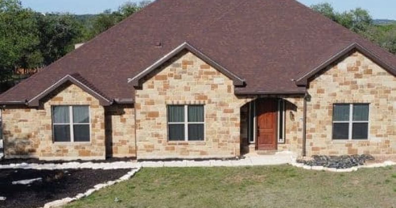 Front view of a single-story, light-brown stone house with a dark reddish-brown metal roof in San Antonio, TX by Dolan Roofing & Construction