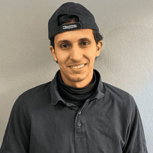 Lächelnder Mann in schwarzer Kleidung und Cap bei Drahtesel Fahrrad.