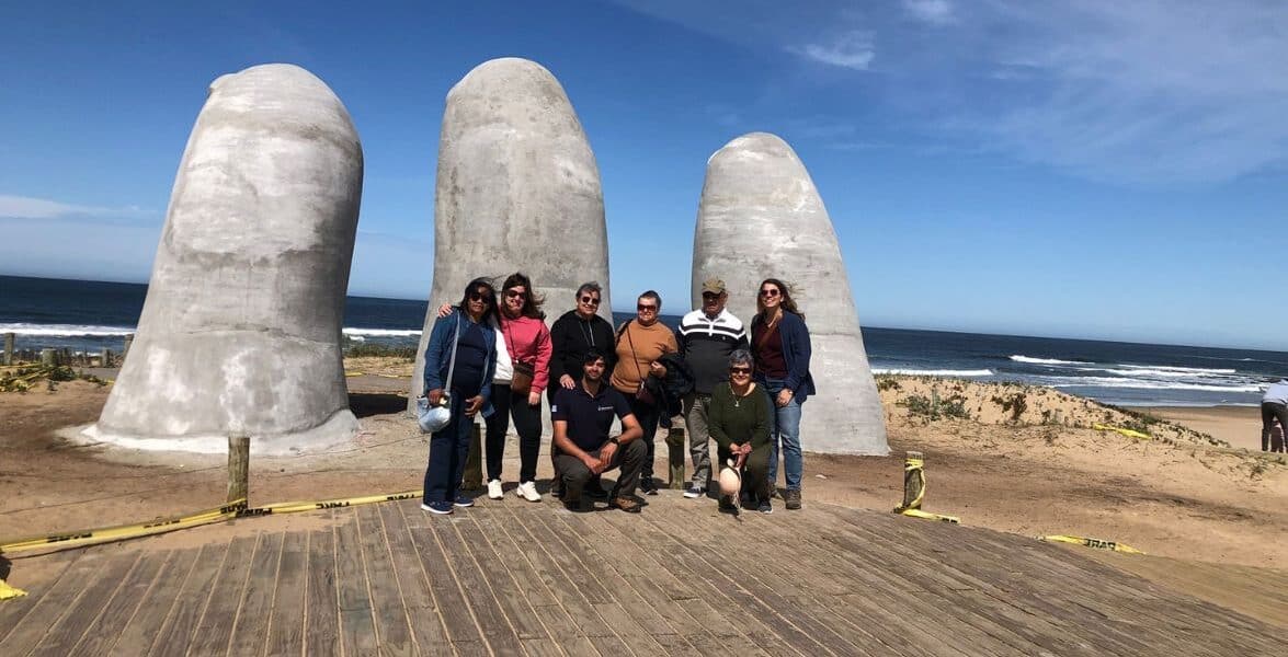 A group of people standing in front of large finger sculptures on a beach.