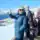 Hiker in winter gear enjoying snowy mountain views with clear blue sky.