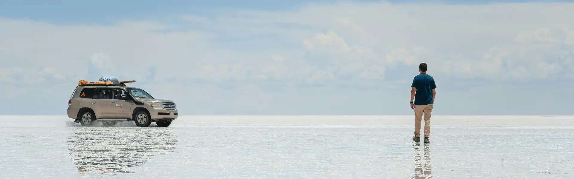 El Kaminante en un paisaje de salinas con un coche y una persona observando el horizonte.