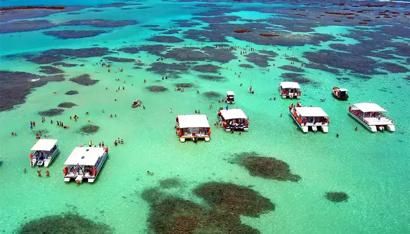 Barcos y turistas en aguas cristalinas y turquesas en un destino turístico costero.