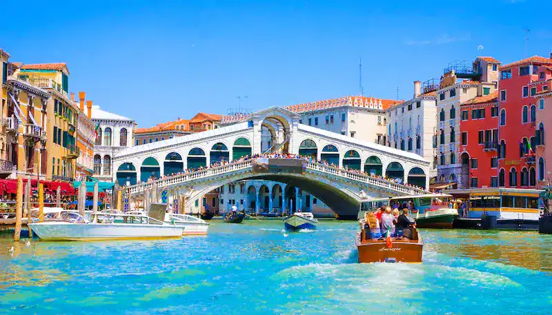 Puente de Rialto en Venecia, Italia, con góndolas y edificios coloridos en el canal.