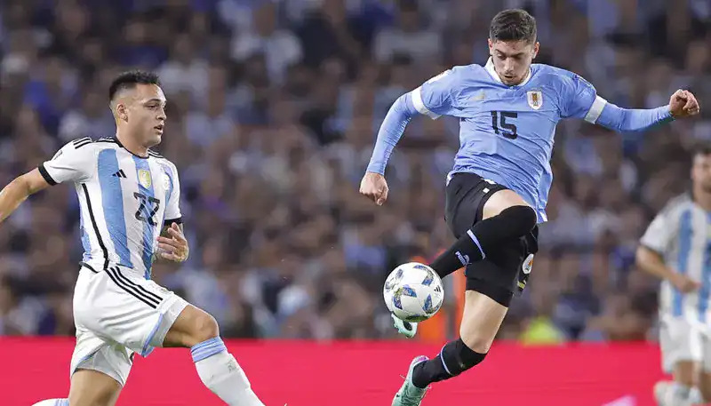 Balón de fútbol en juego durante partido entre Argentina y Uruguay en un estadio.