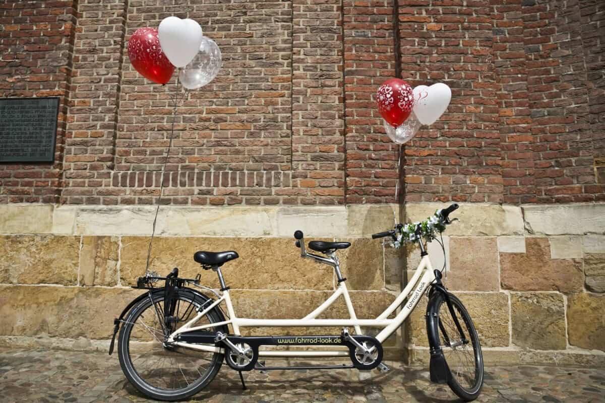 Doppeltes Fahrrad mit Herz- und Ballon-Dekoration vor Backsteinmauer in Münster.