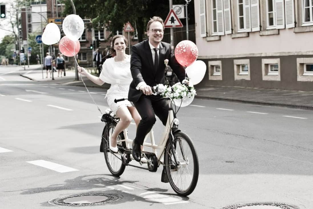 Paar fährt auf Fahrrad mit Ballons durch Münster bei Hochzeit.