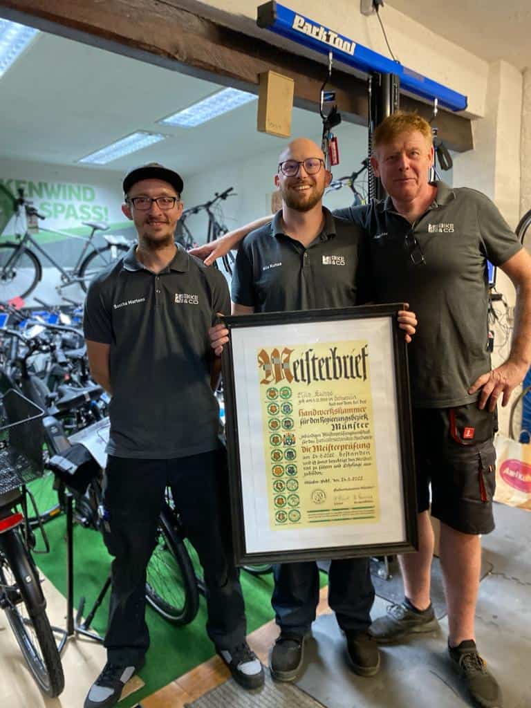 Drei Mitarbeiter von Fahrrad Kuhse Güstrow präsentieren eine Urkunde im Fahrradladen.