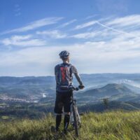 Fahrradservice Winkler | Templin Radfahrer mit Mountainbike auf Berggipfel mit Blick auf Täler.