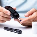 High-quality image of a person using a blood glucose meter for diabetes testing, with test strips and a lancing device on a white surface, highlighting healthcare and medical testing.