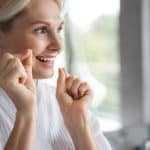 Dental patient smiling with dental floss, emphasizing oral hygiene and dental care services.
