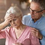 Overwhelmed senior woman with headache being comforted by her adult son, highlighting legal issues related to elder care or guardianship services.