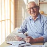Elderly man smiling with tablet in a cozy home setting, representing legal services for seniors and estate planning from Farr Law Firm.