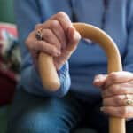 Close Up Of Senior Woman Sitting In Chair Holding Walking Cane