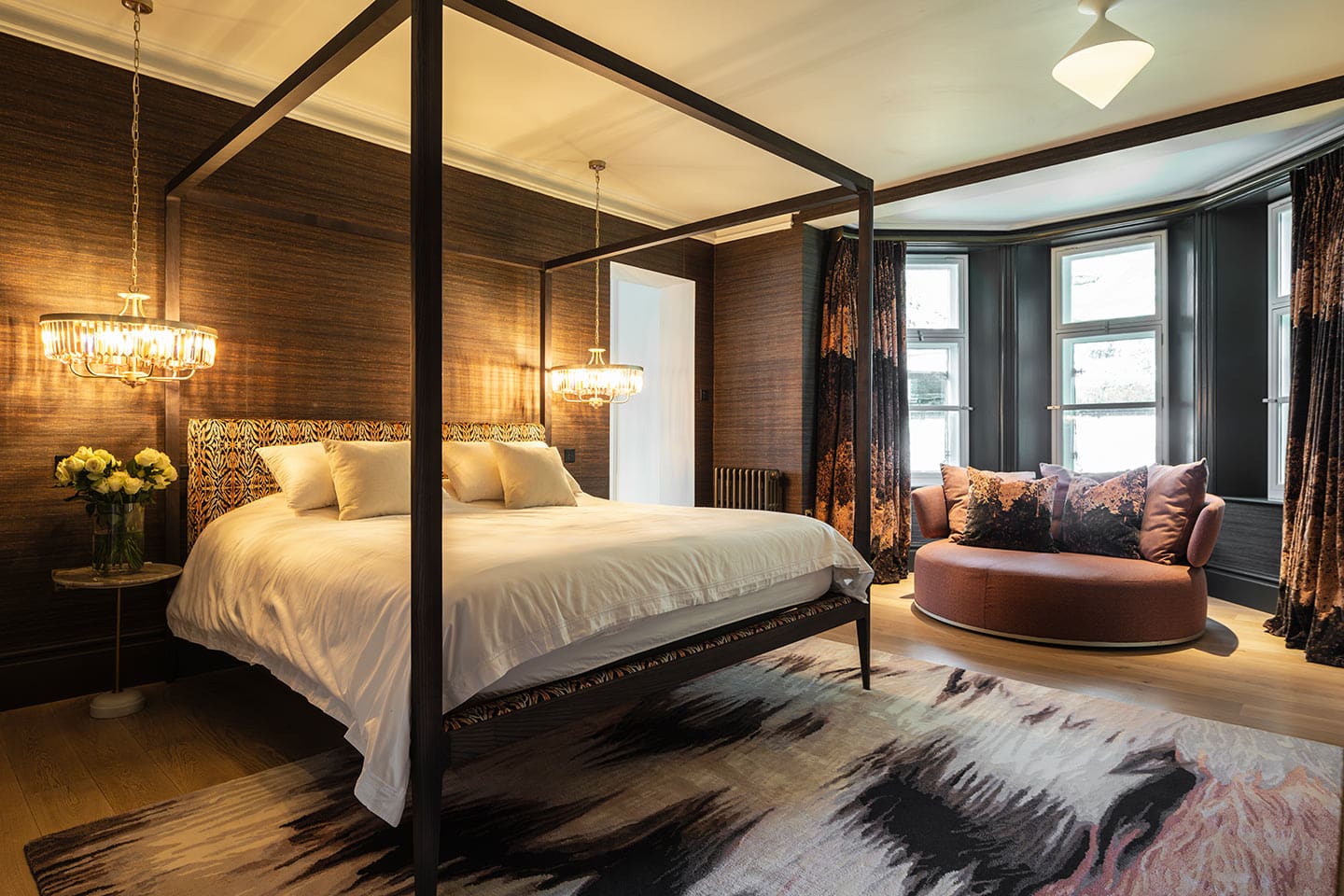 Elegant master bedroom with a four-poster bed, cosy seating area, and warm lighting.
