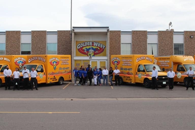 A group of people stands in front of a building labeled "Golden West" with several yellow company vans parked outside, giving a glimpse into the team behind our story on the About Us page.