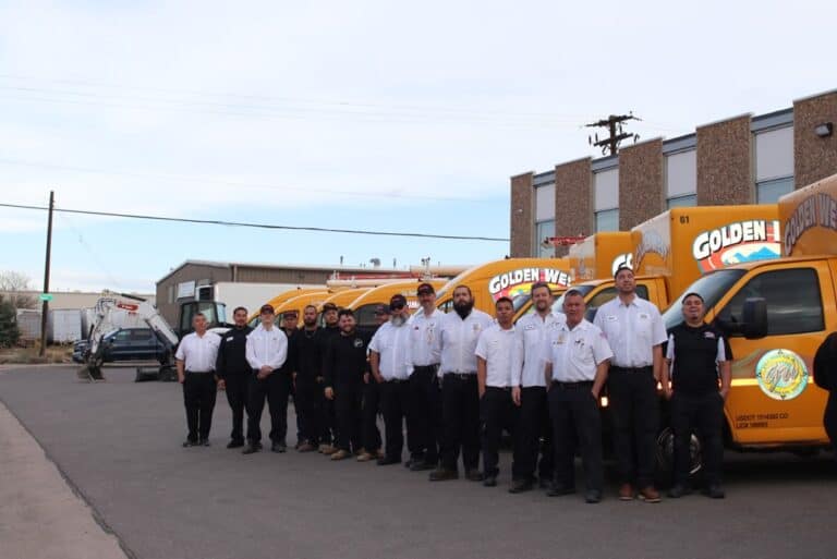 A group of uniformed workers stands in front of a row of yellow company vans in a parking lot outside an industrial building, reflecting the teamwork and dedication found on our About Us page.