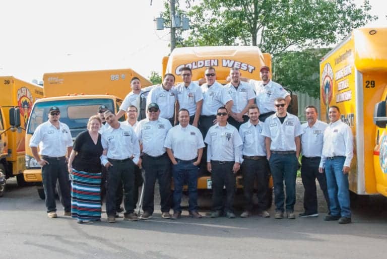 A group of 17 people, mostly men in white shirts and dark pants, poses in front of yellow service trucks outdoors on a sunny day, ready to earn positive customer reviews.