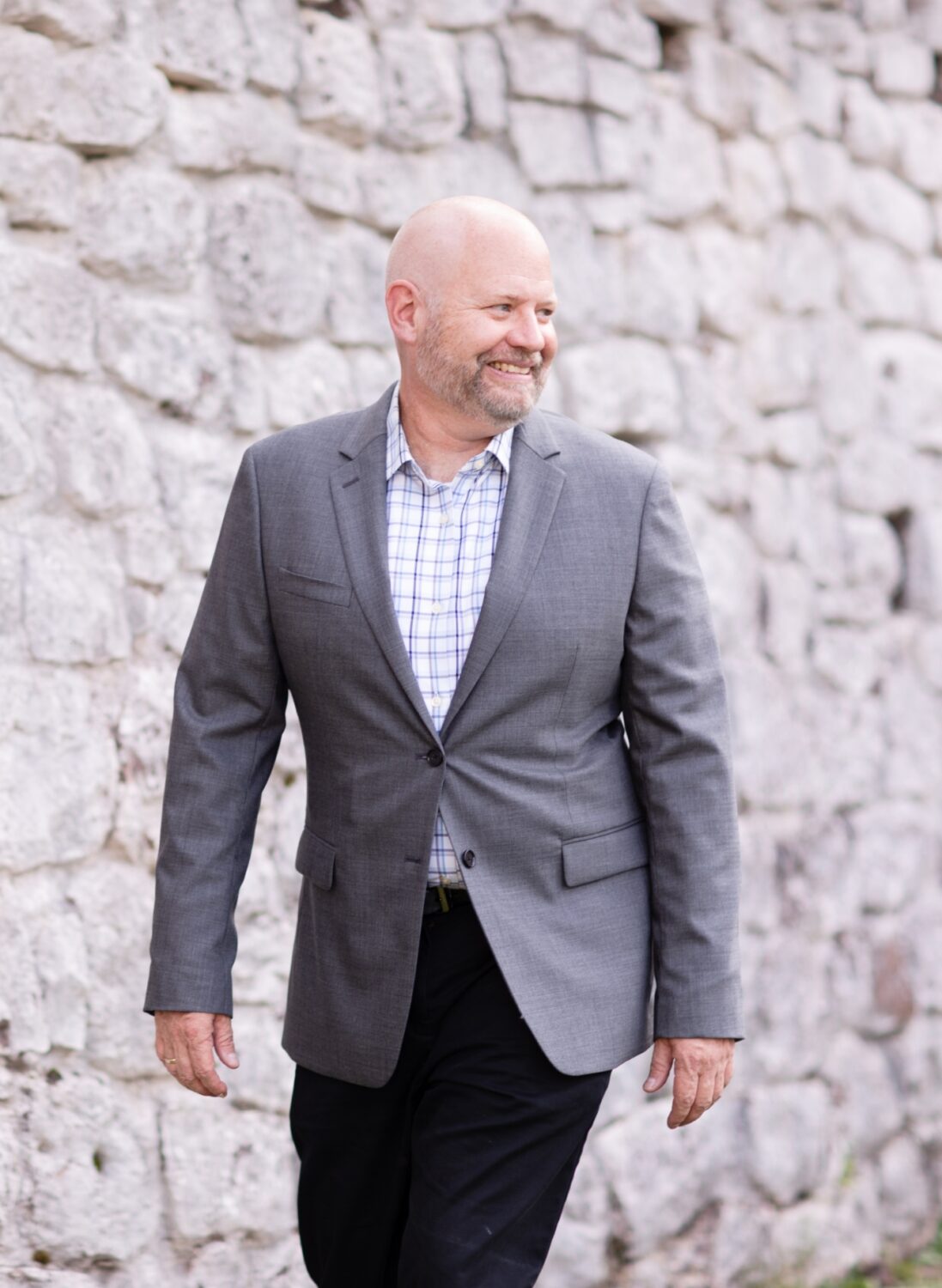 Jim White, owner of Great Oak Wealth Management, smiling while walking in front of a stone wall