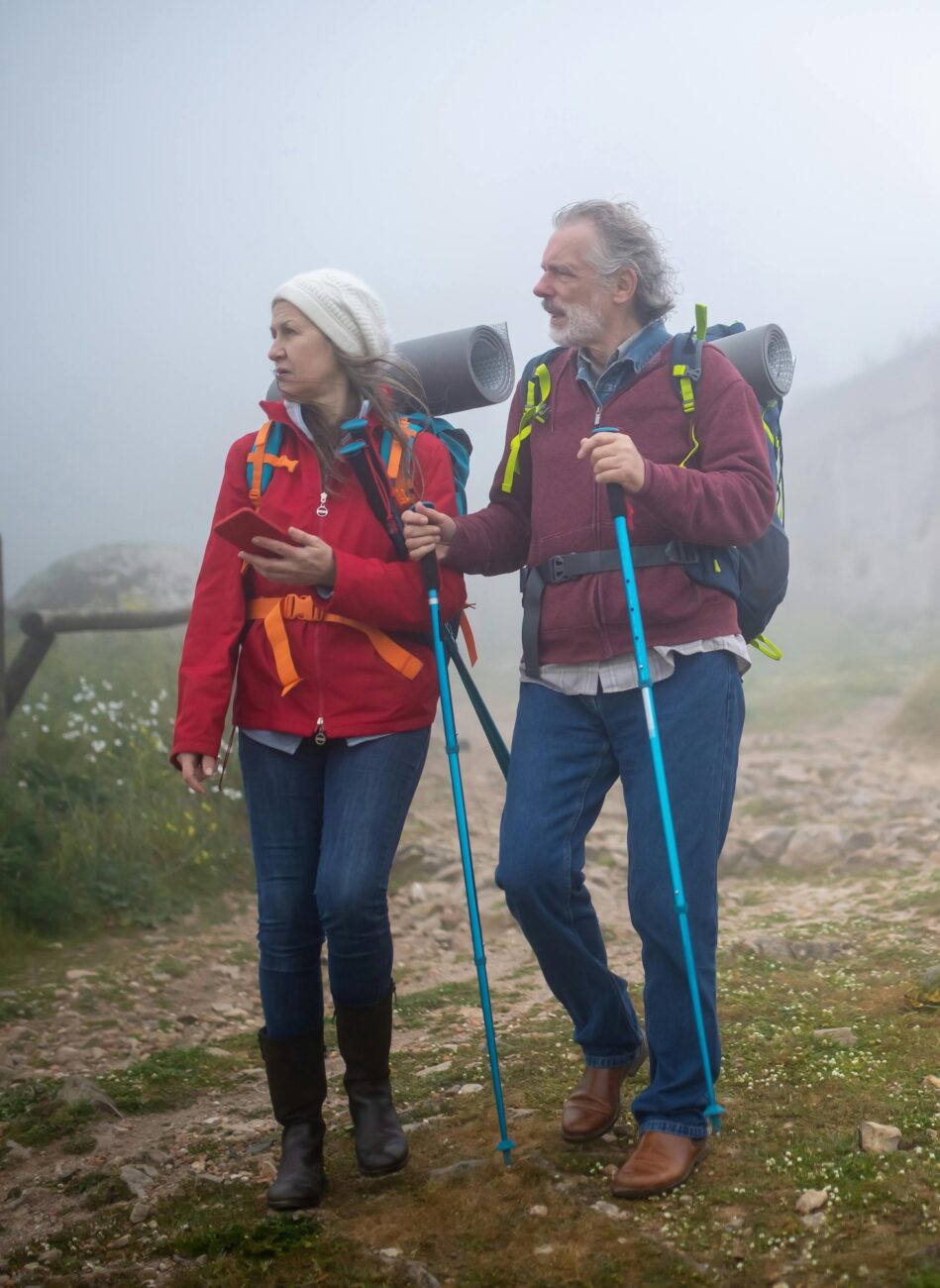 Older couple hiking with backpacks and walking sticks on a foggy trail