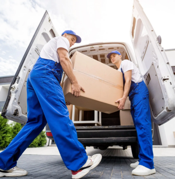 Two movers loading a large box into a moving van in a residential area.