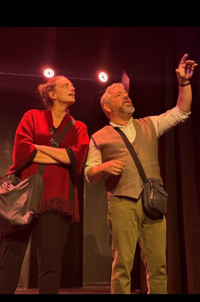 Two people pointing on stage under spotlights.