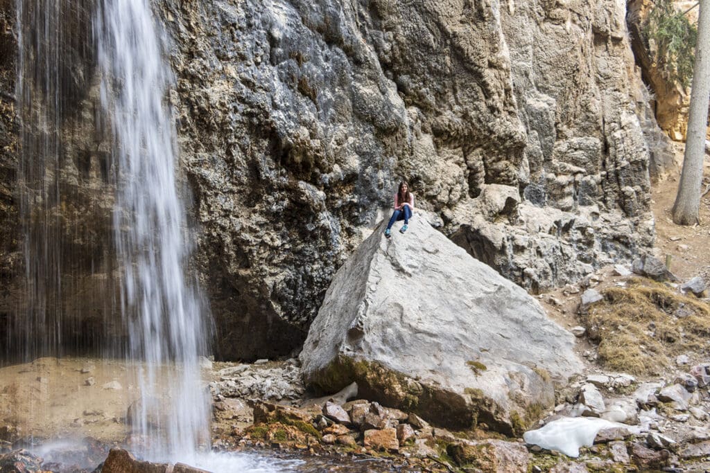 Hiking Hanging Lake in Colorado – The Ultimate Guide Another view of spouting rock with a girl sitting on a large boulder nearby.