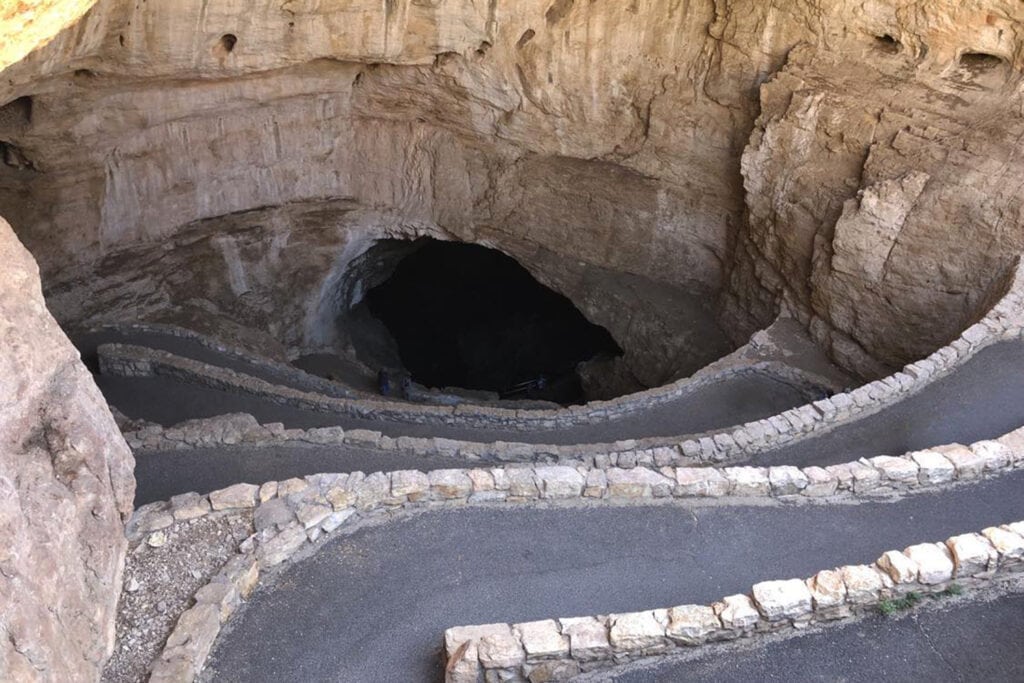 Discover the Funnest National Parks for Kids Entrance to Carlsbad Caverns, a natural wonder. The rocky path leading into the cave, showcases the park's captivating geological formations.
