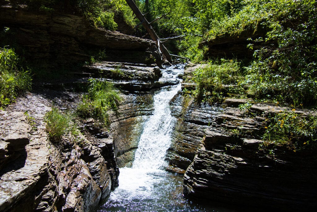 Your Ultimate Guide To Hiking Devil’s Bathtub SD Captivating image of Devil's Bathtub natural waterslide in Spearfish Canyon. Crystal-clear water cascading down smooth rock formations, inviting adventure and exploration.