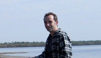 Man by water with scenic lake background, enjoying nature.