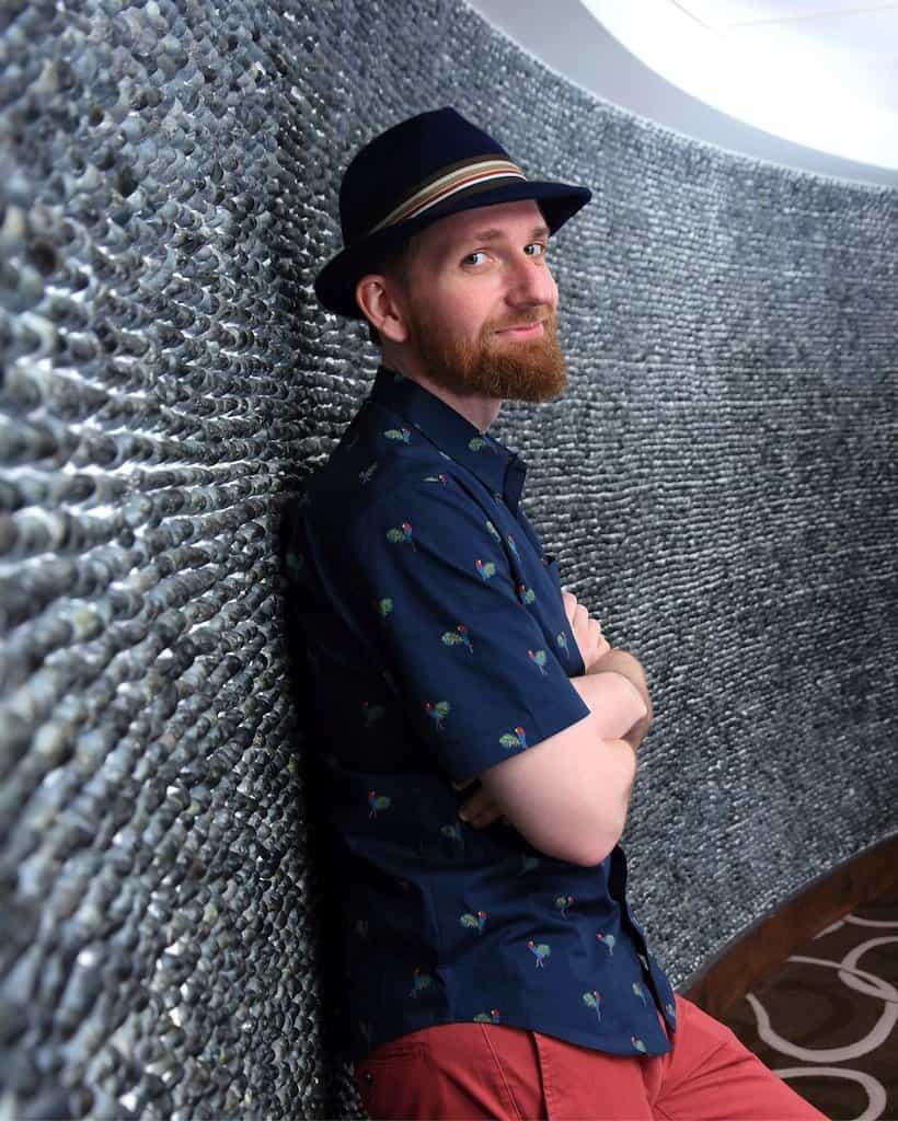 Stylish man with hat leaning against textured wall at Hero Initiative event.