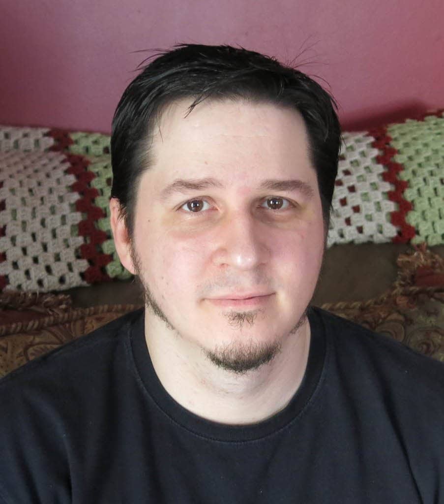 Portrait of a man with dark hair and beard, sitting in a cozy home environment.