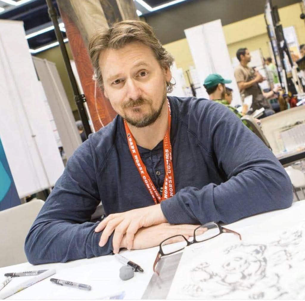 Close-up of a man at an art convention, showcasing illustrations, with a focus on creativity and charity art events.
