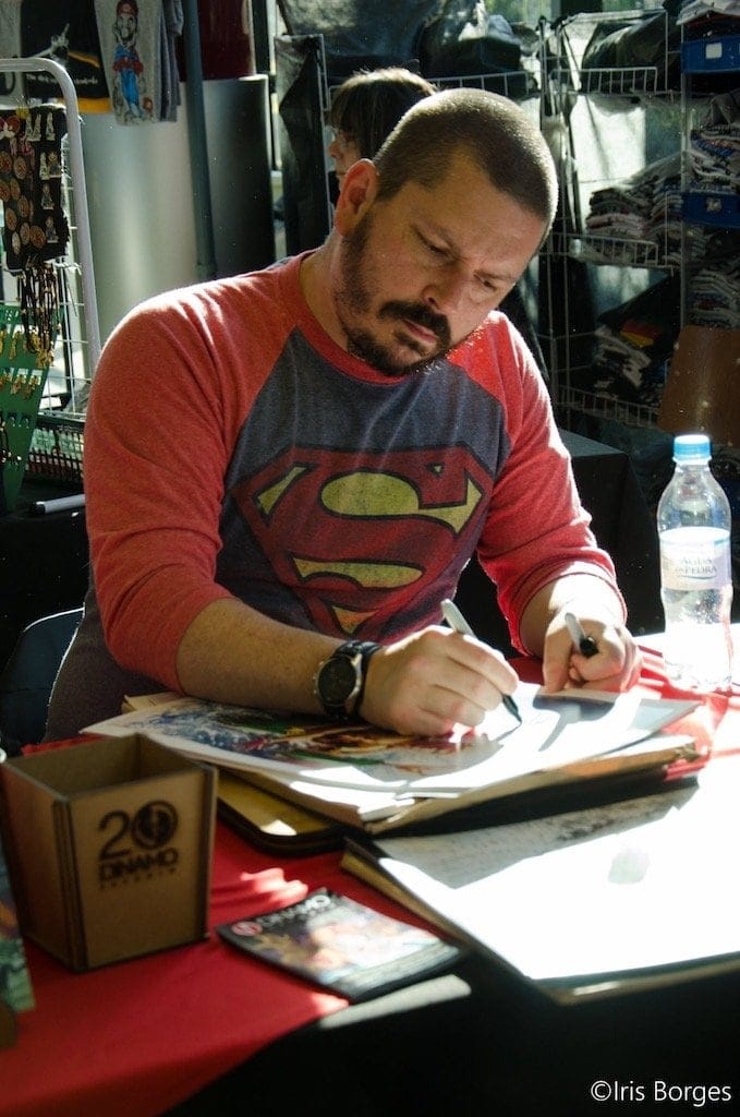 Comic artist signing artwork at charity event for superheroes' financial support.