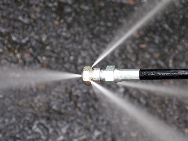 Close-up of a pressure washer nozzle spraying water in five streams against a dark, wet surface.